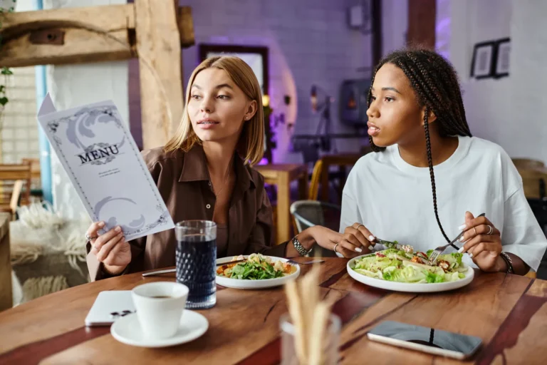 Two diners at a restaurant table looking toward a menu, with salads and drinks in front of them.