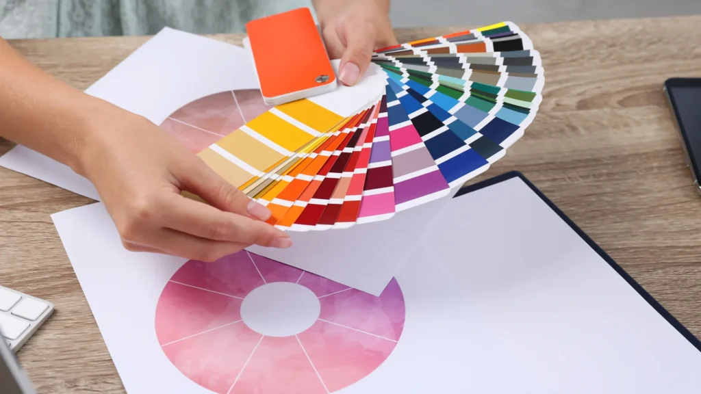 Hands hold a fan of color swatches above printed circular color charts on a desk.