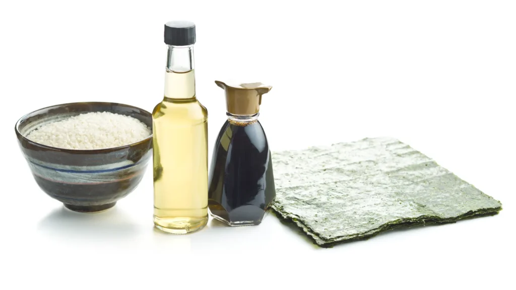 Rice vinegar and soy sauce bottles beside a bowl of rice and sheets of nori