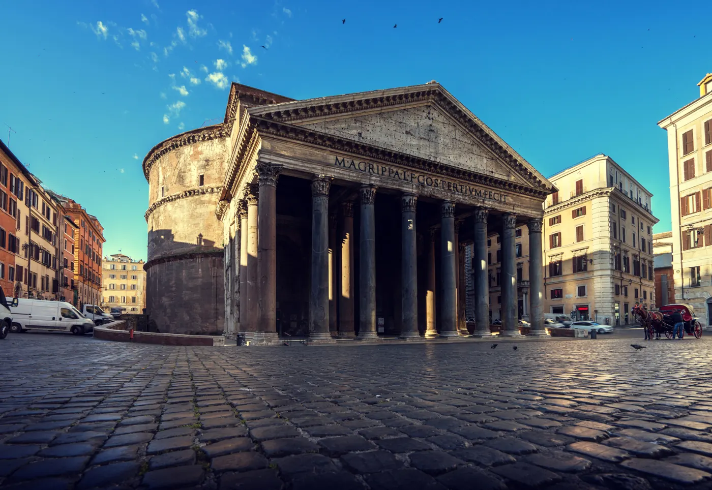 Wide view of the Pantheon’s portico and round exterior with cobbled paving and neighboring buildings
