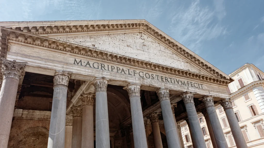 Upward view of the Pantheon’s stone columns, triangular pediment, and inscription beneath a pale blue sky