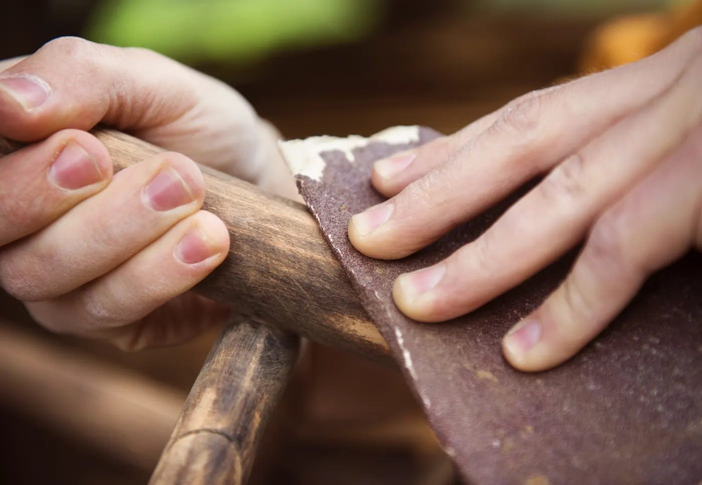 Hands holding sandpaper against the surface of a wooden piece