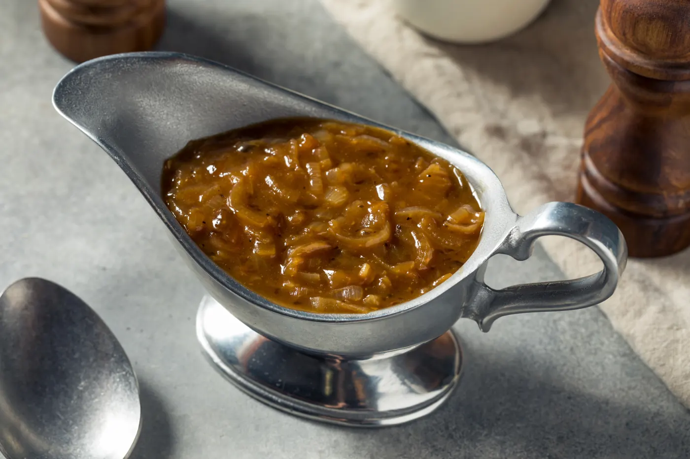 Brown onion gravy fills a silver-colored gravy boat beside a serving spoon.