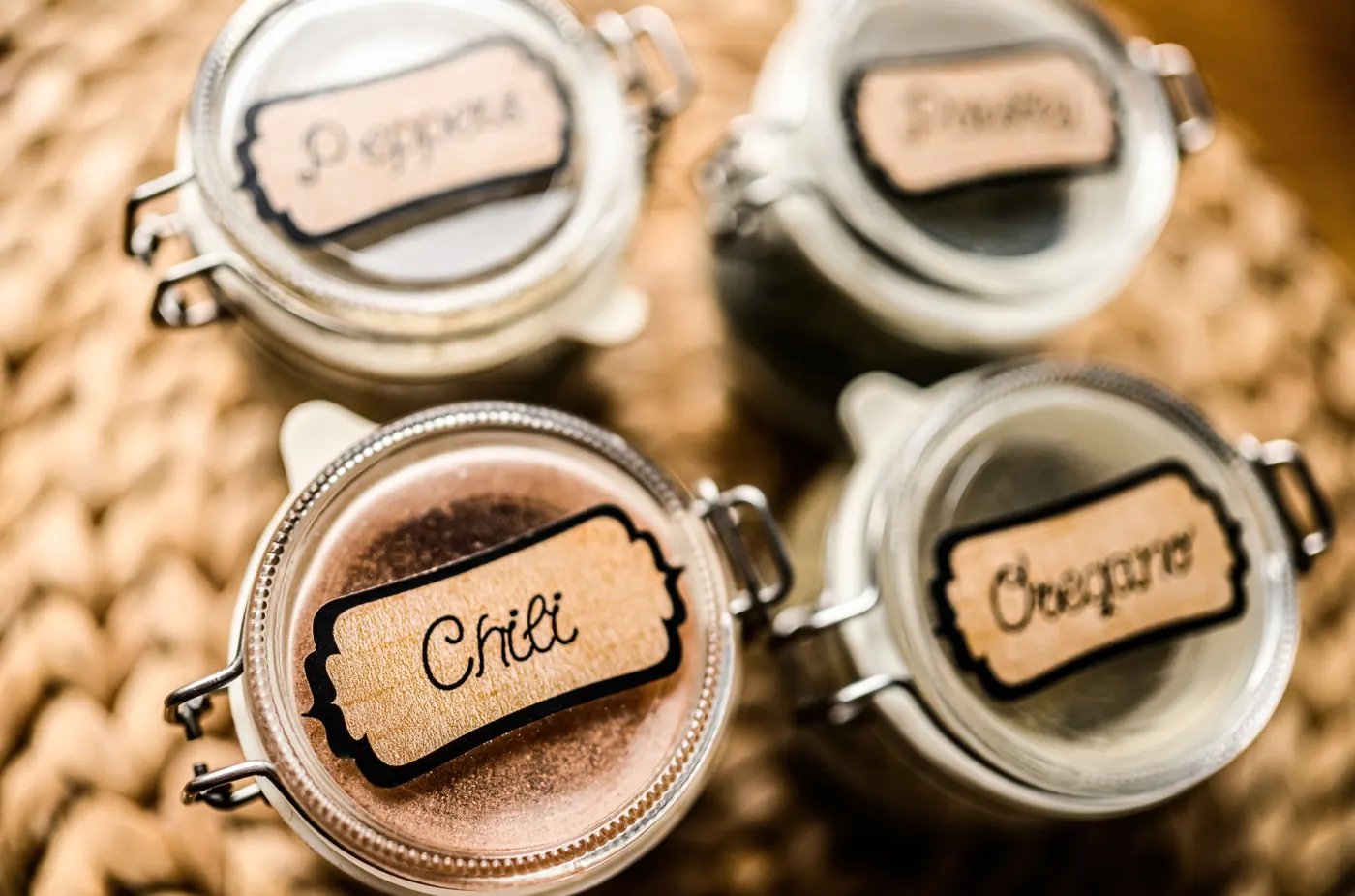 Glass spice jars with handwritten labels, including chili and oregano, viewed from above.