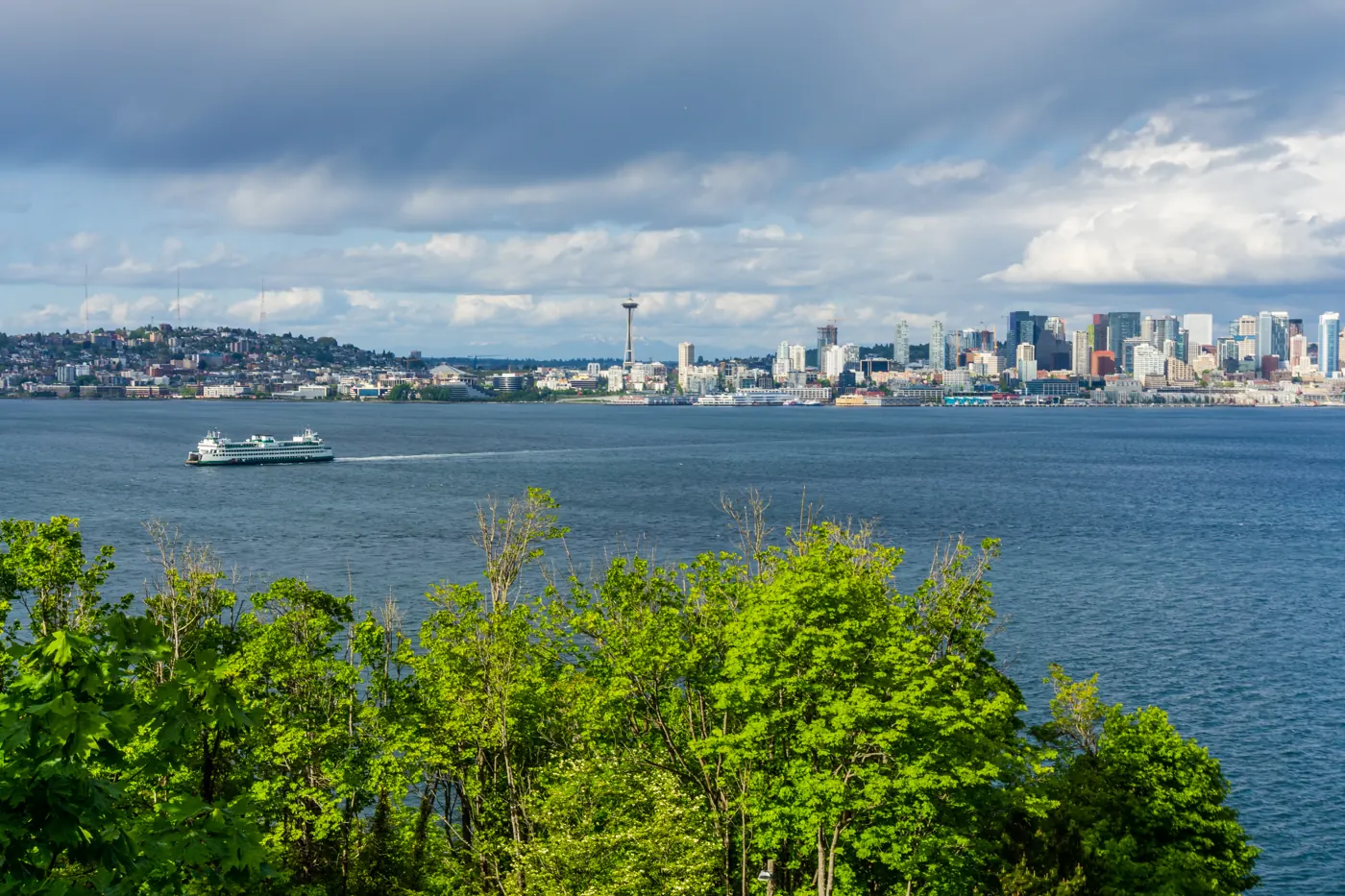 A ferry crossing the water in front of the Seattle skyline with green foliage in the foreground