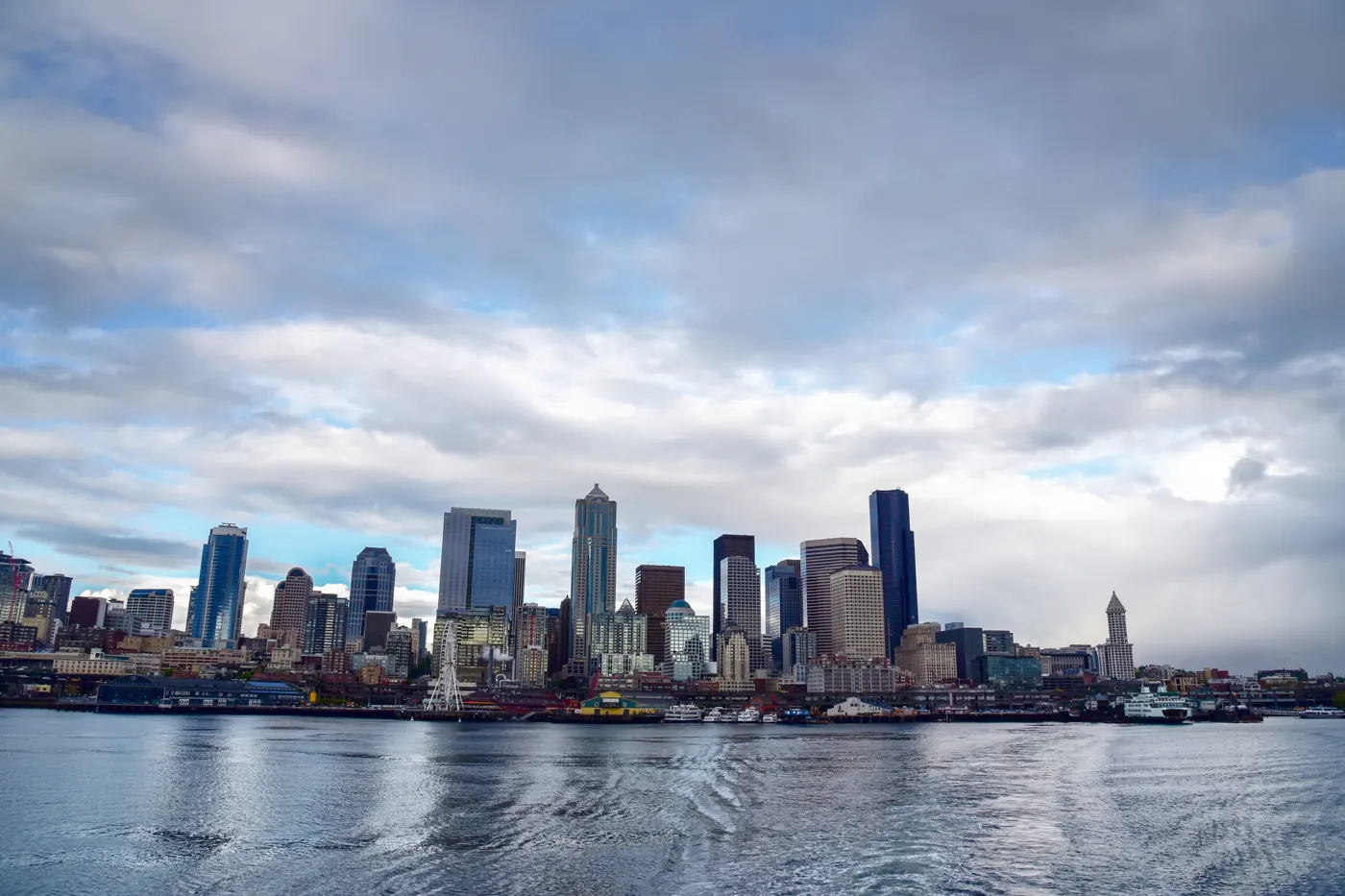 Seattle waterfront skyline viewed across water and a ferry wake beneath a cloudy sky