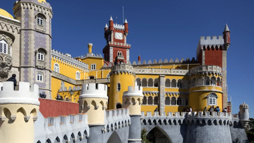 Red and yellow towers, arched terraces, and stone walls at Pena Palace in Sintra beneath a blue sky