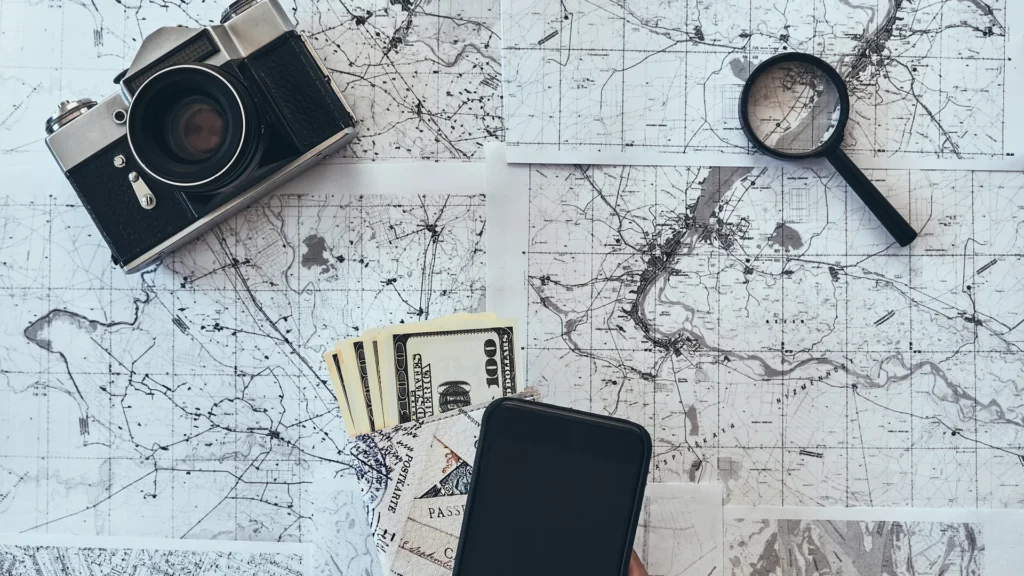 A travel map with a camera, compass, and smartphone arranged for planning.