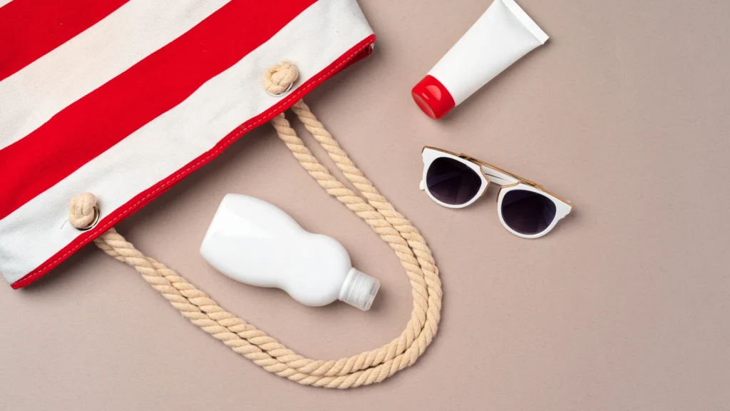 A striped beach bag, sunglasses, and sunscreen arranged for a day outside.