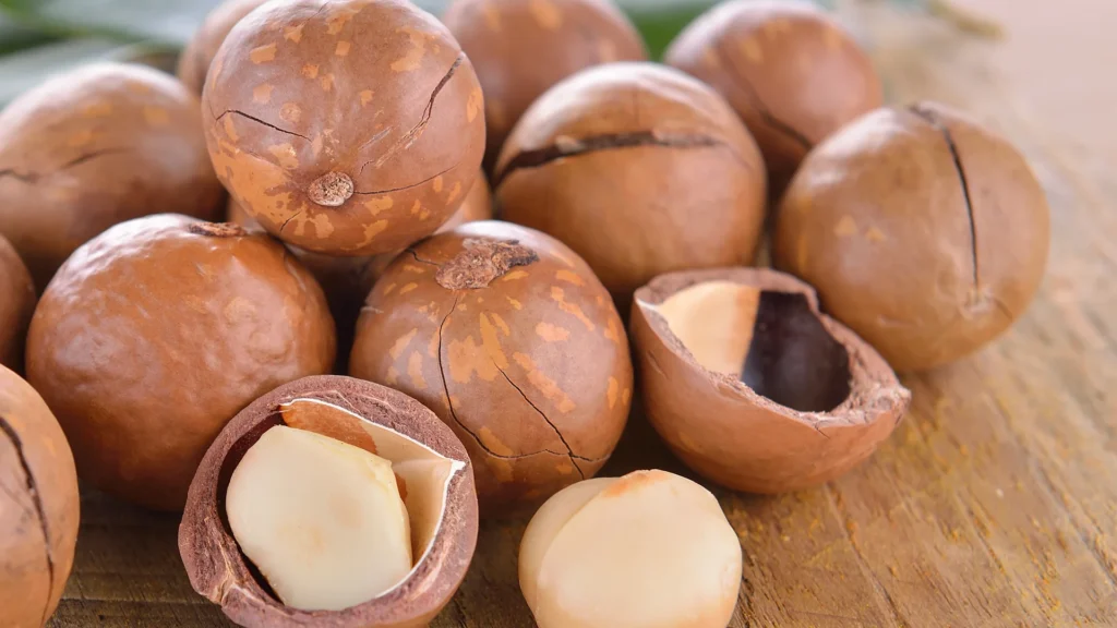 Shelled and unshelled macadamia nuts on a wooden surface.