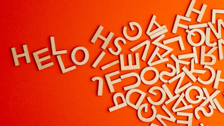 Wooden letter shapes scattered on an orange surface, with letters arranged to spell hello.