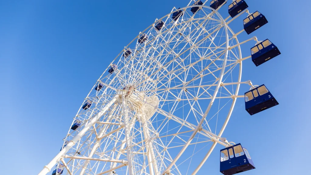 A Ferris wheel with blue gondolas against a clear sky.