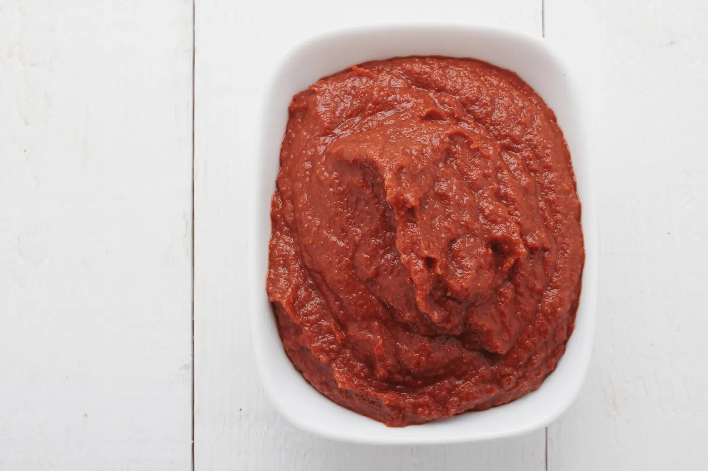Dense red tomato paste in a white rectangular bowl on a pale wooden surface