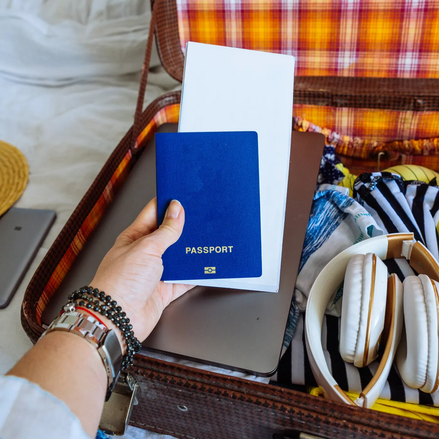 A hand holding a closed passport and a white document over an open suitcase.