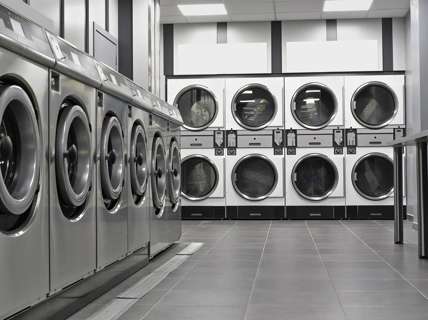 Rows of front-loading laundry machines in an empty tiled room