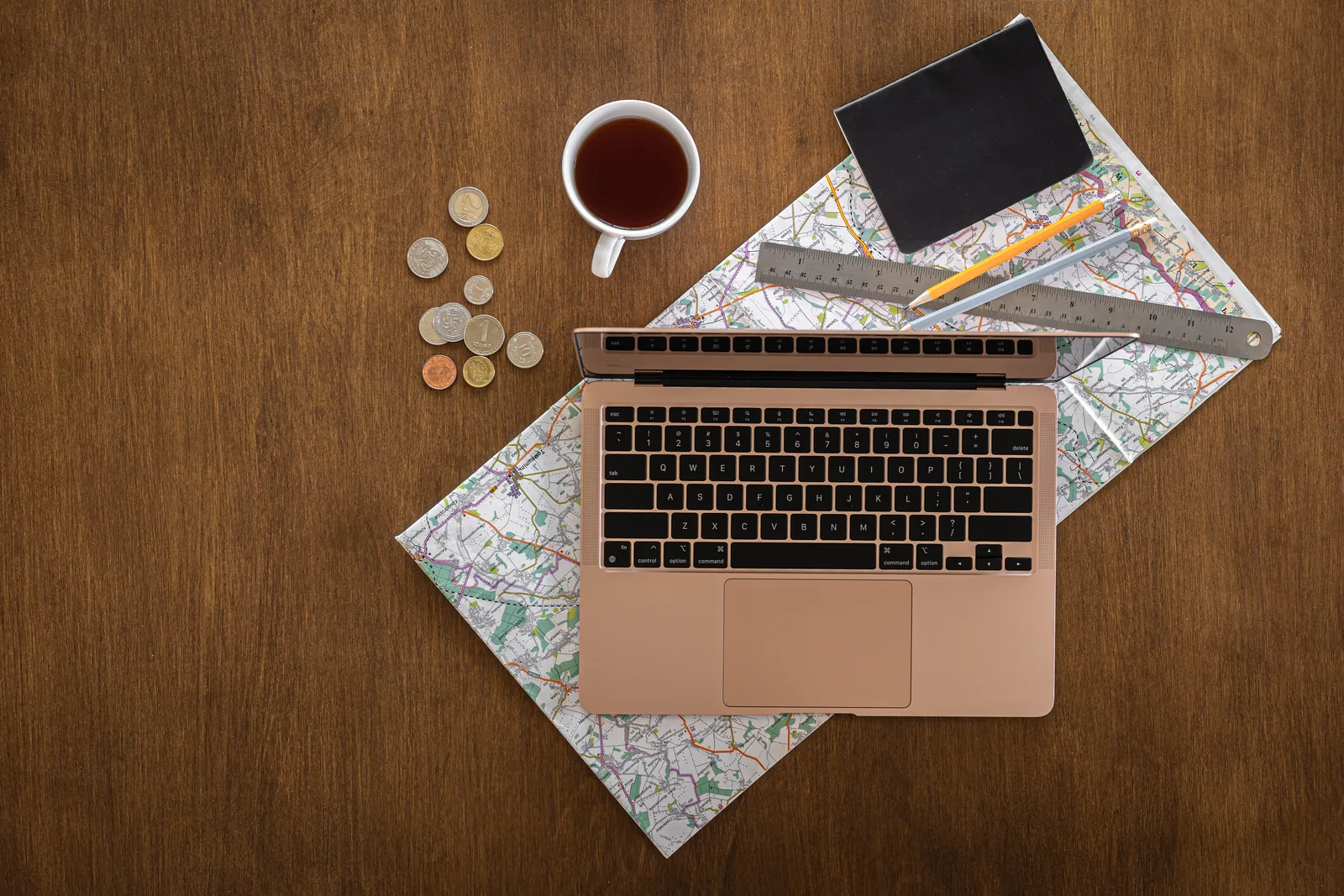 A laptop, map, and travel accessories arranged on a wooden table.