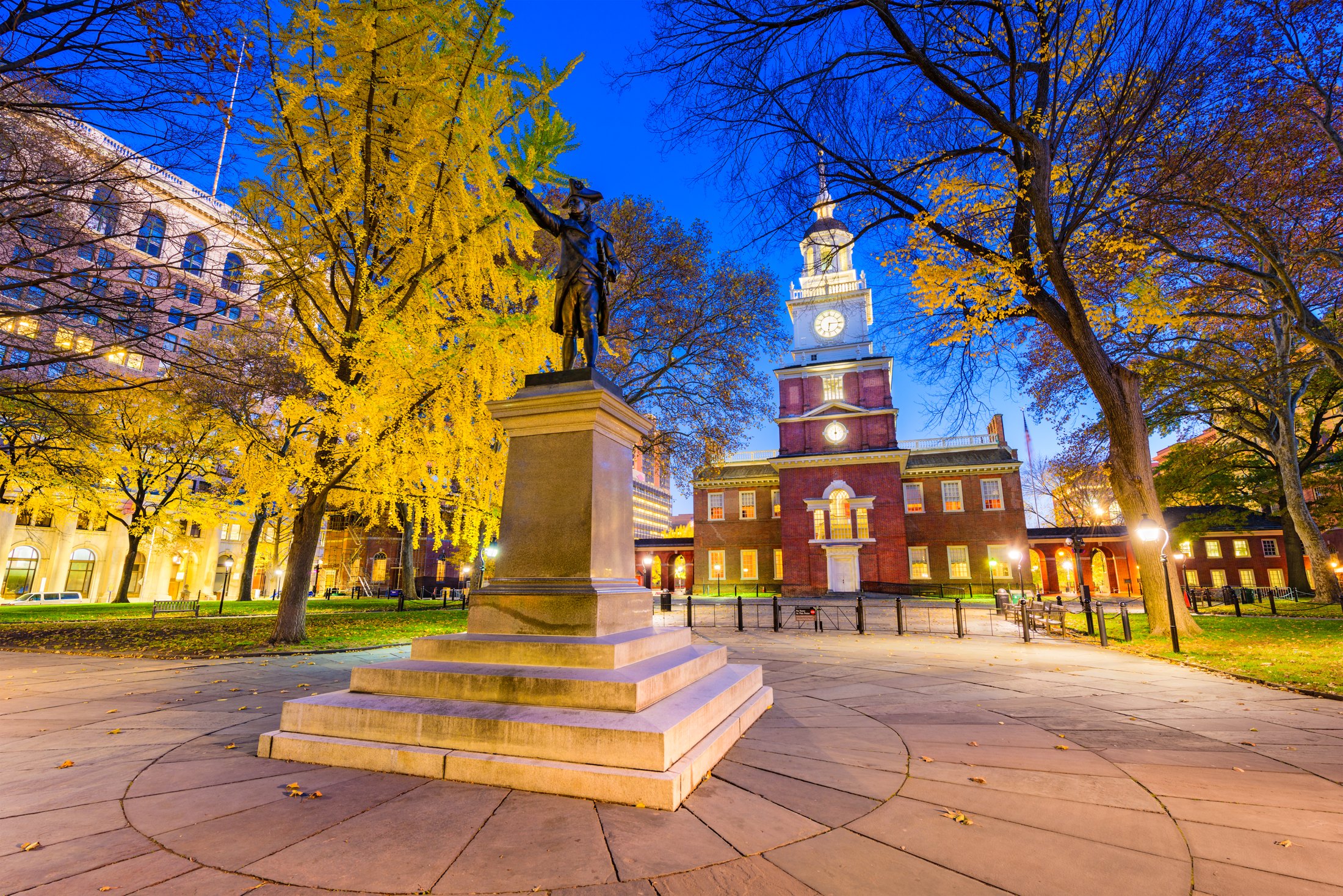 Independence Hall’s illuminated brick facade and clock tower behind the George Washington statue in Philadelphia