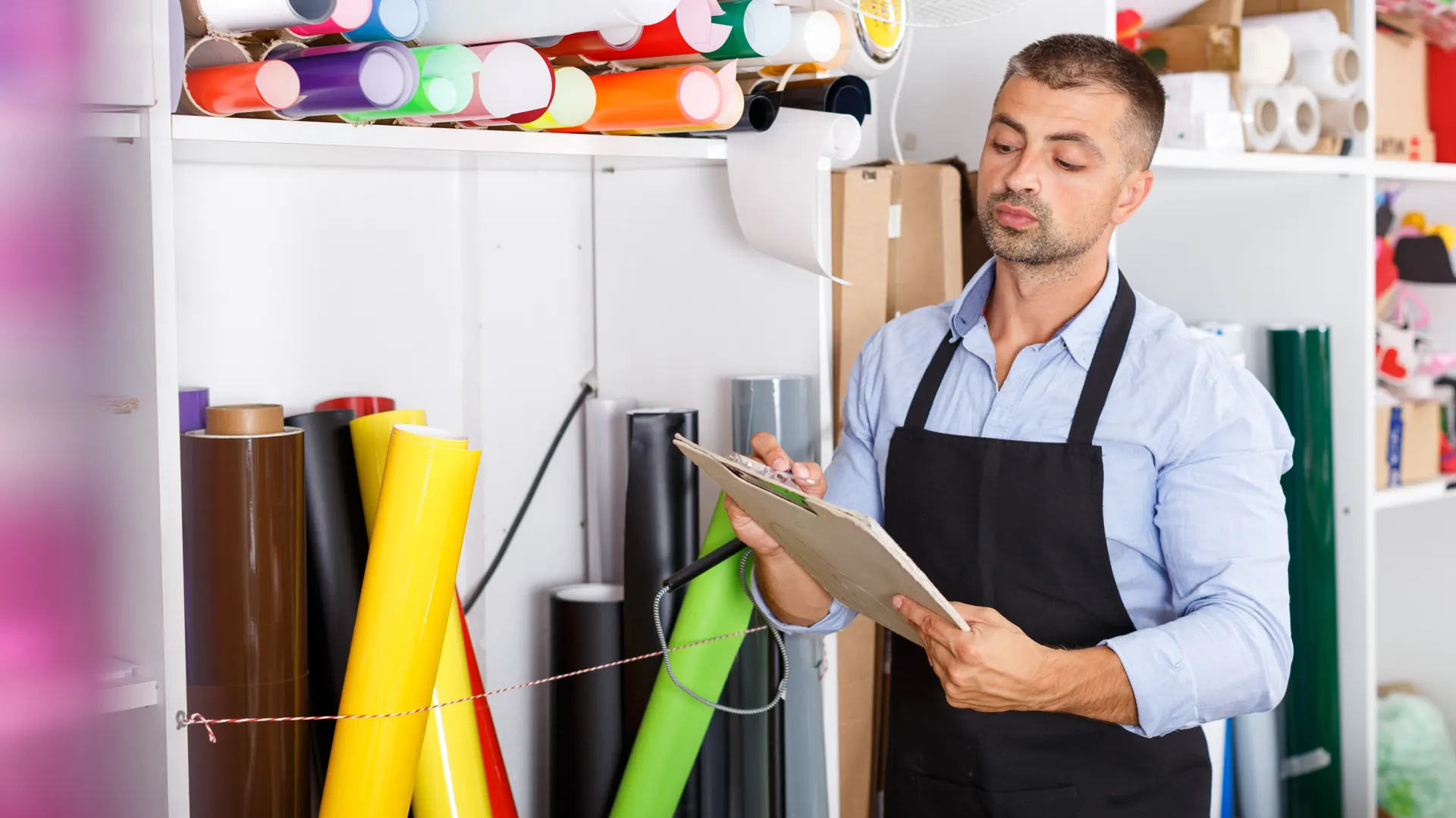 A worker holds a clipboard beside upright and shelved rolls of colored vinyl.