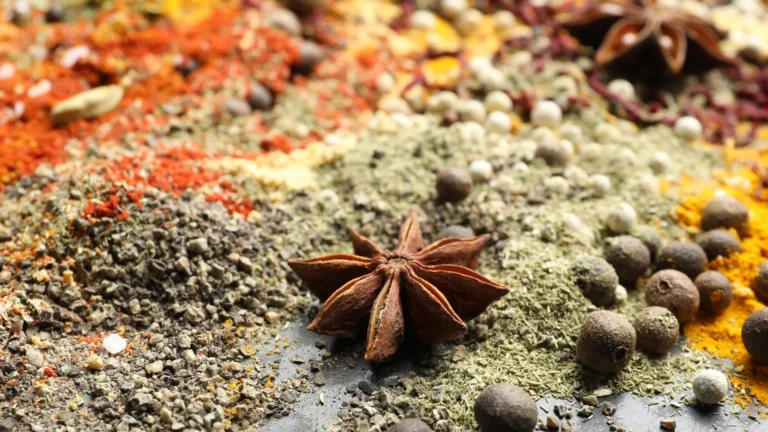 Whole star anise and peppercorns beside ground spices on a dark surface.