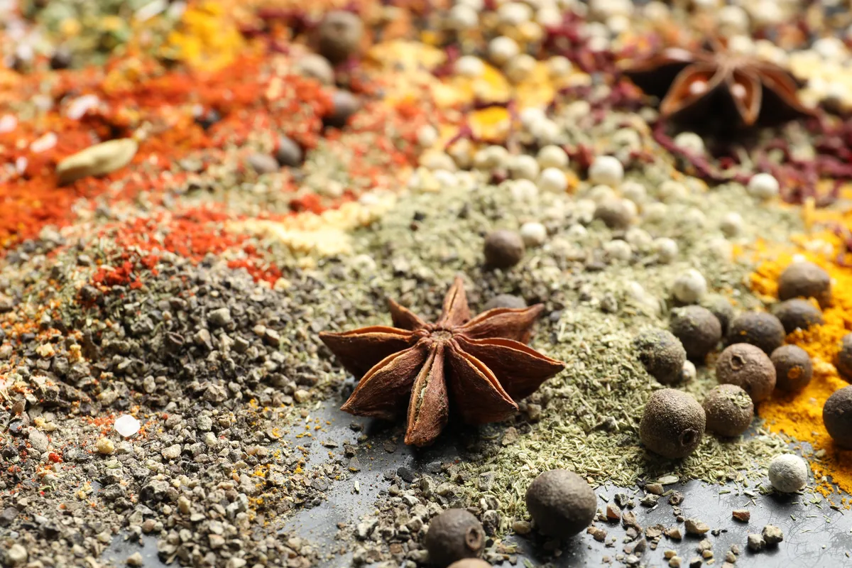 Whole star anise and peppercorns beside ground spices on a dark surface.