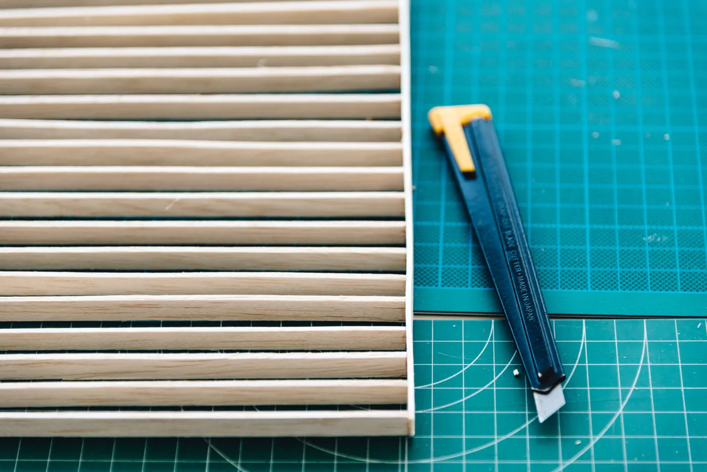 A utility knife and a model with parallel wooden strips on a green cutting mat.