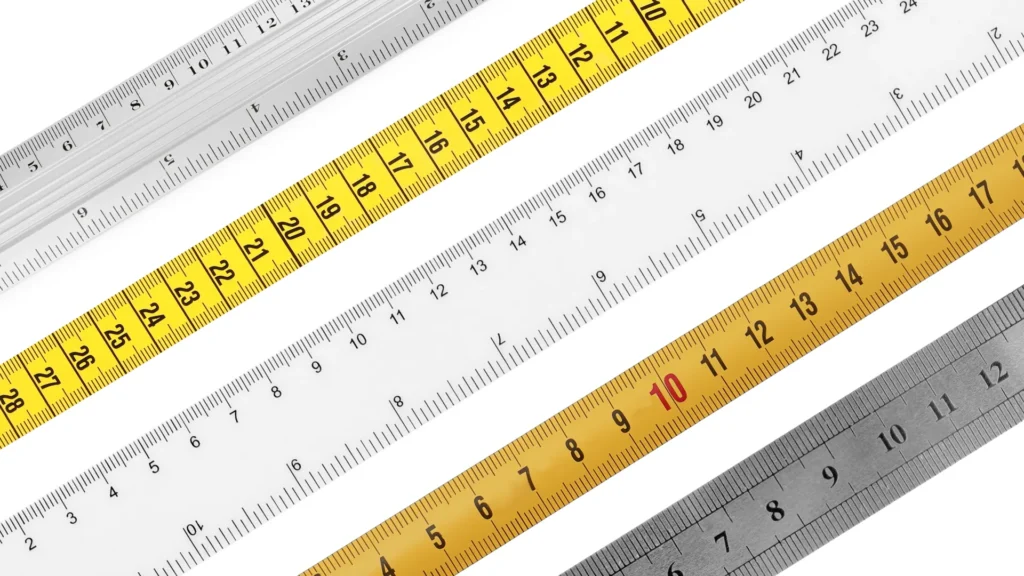 Several transparent, yellow, and metal rulers arranged diagonally on white