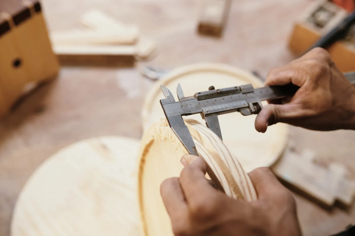 Hands holding a wooden piece while measuring its thickness with calipers.
