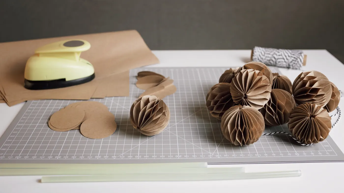 Kraft-paper circles and honeycomb paper balls with scissors and a punch on a gridded mat.