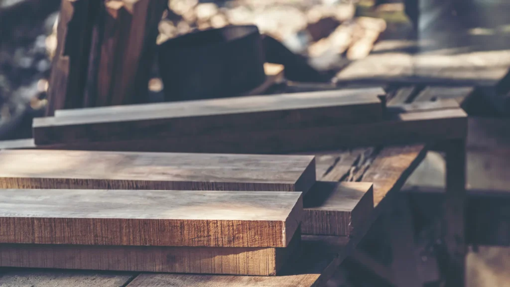 Thick brown timber boards lie stacked across a wooden workbench in a workshop.
